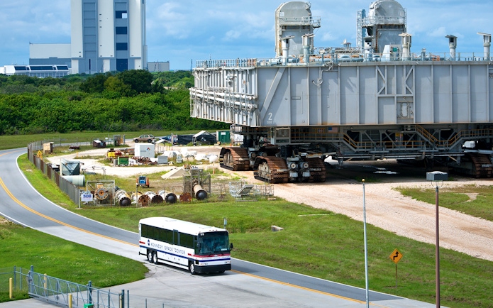 Kennedy Space Center bus near a large crawler-transporter with a launch pad in the background.