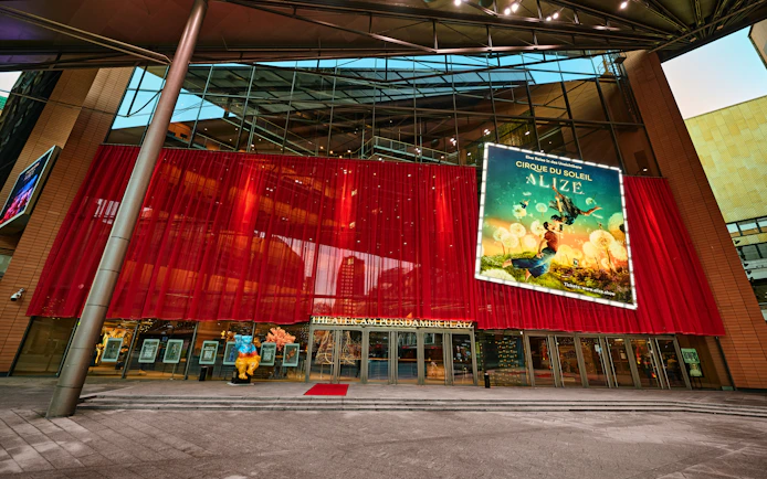 Exterior view of Cirque du Soleil Alizé Theatre with red drapes and promotional poster.