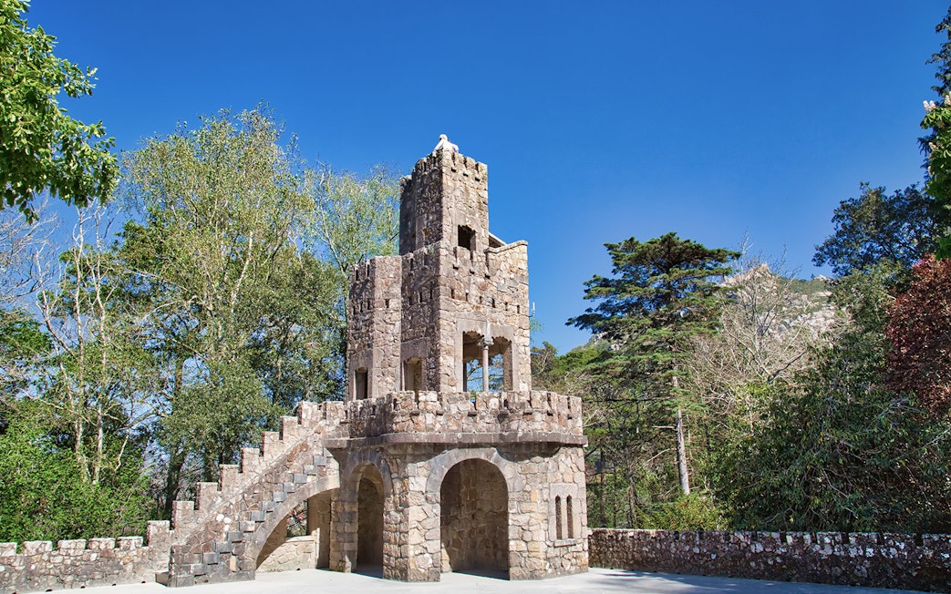 Stone tower with spiral staircase at Quinta da Regaleira Palace, Sintra, surrounded by trees.