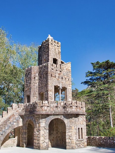 Stone tower with spiral staircase at Quinta da Regaleira Palace, Sintra, surrounded by trees.