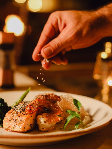 Hand sprinkling salt on gourmet dish at premium dining safari experience.