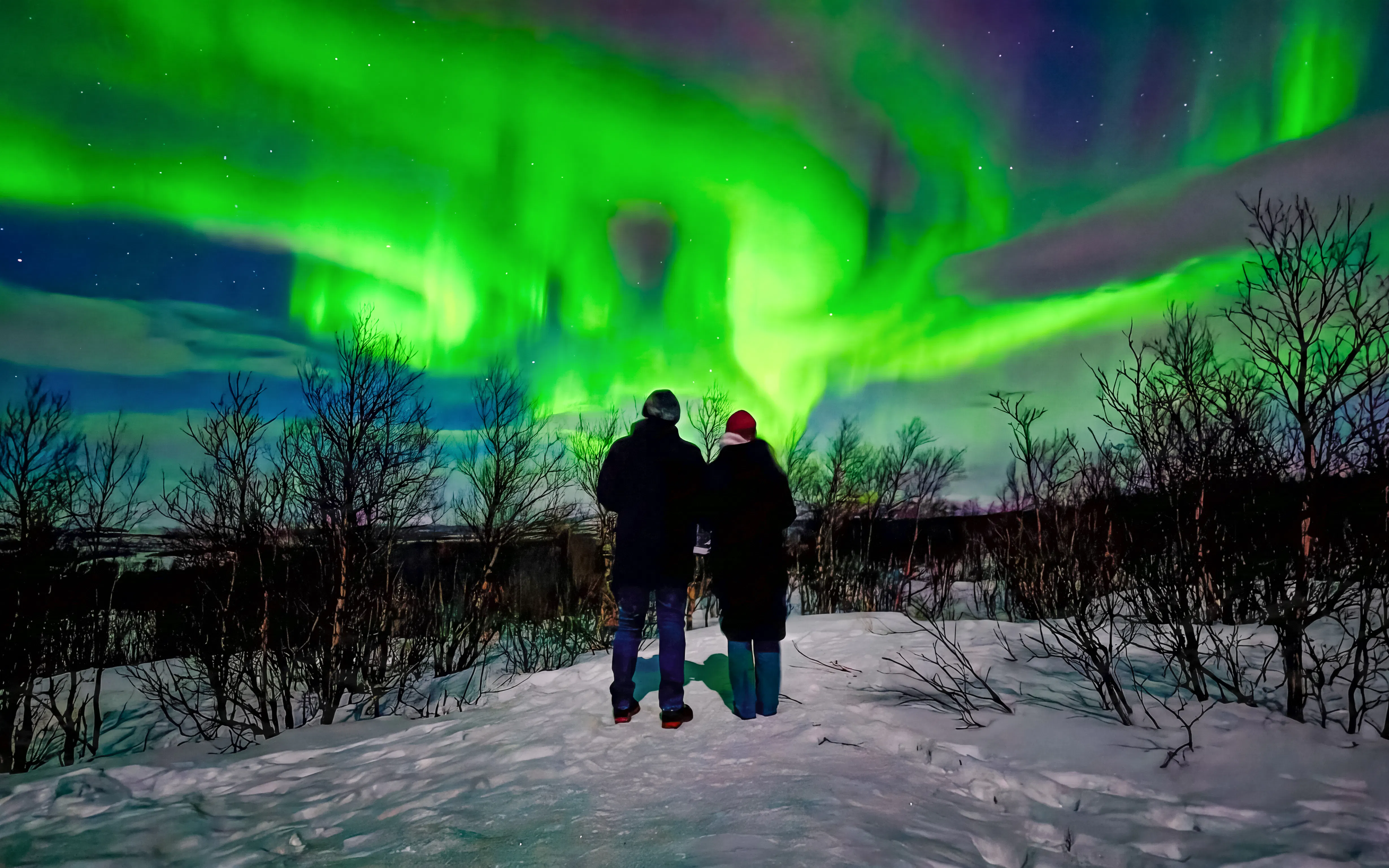 Couple viewing northern lights in snowy Kiruna landscape.