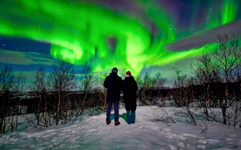 Couple viewing northern lights in snowy Kiruna landscape.