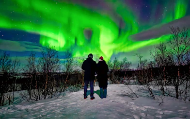 Couple viewing northern lights in snowy Kiruna landscape.