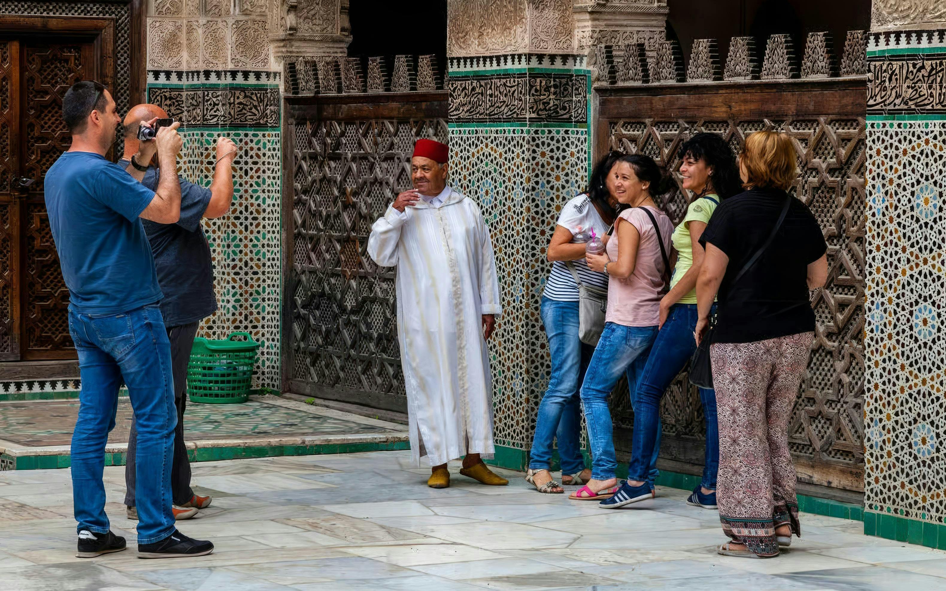 Visitors at Al Attarine Madrasa in Fes, Morocco, admire intricate tilework.