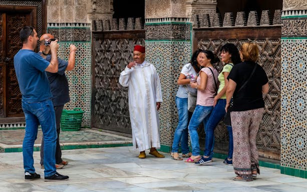 Visitors at Al Attarine Madrasa in Fes, Morocco, admire intricate tilework.