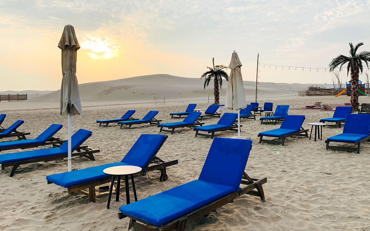 Sunset view of blue lounge chairs on sandy beach at Al Majles Resort.