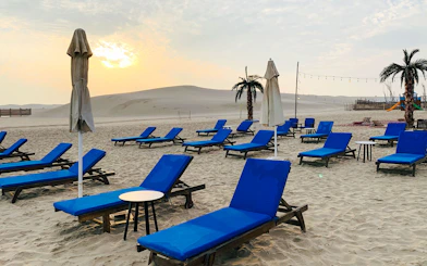 Sunset view of blue lounge chairs on sandy beach at Al Majles Resort.