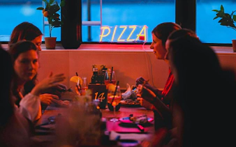 Group dining on a pizza cruise with neon sign and drinks.