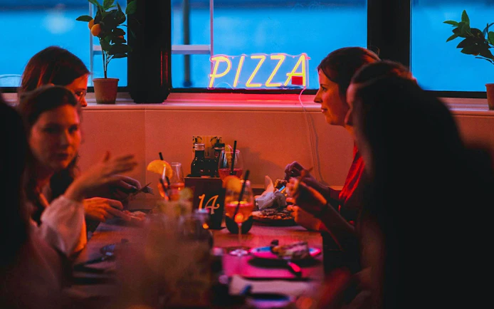 Group dining on a pizza cruise with neon sign and drinks.