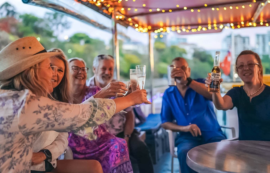 Friends toasting drinks on a Brisbane River cruise boat.