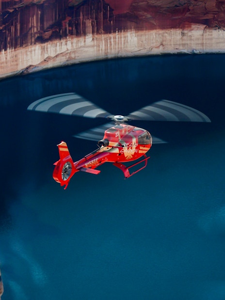 Red Papillon helicopter flying over Lake Powell's blue waters.