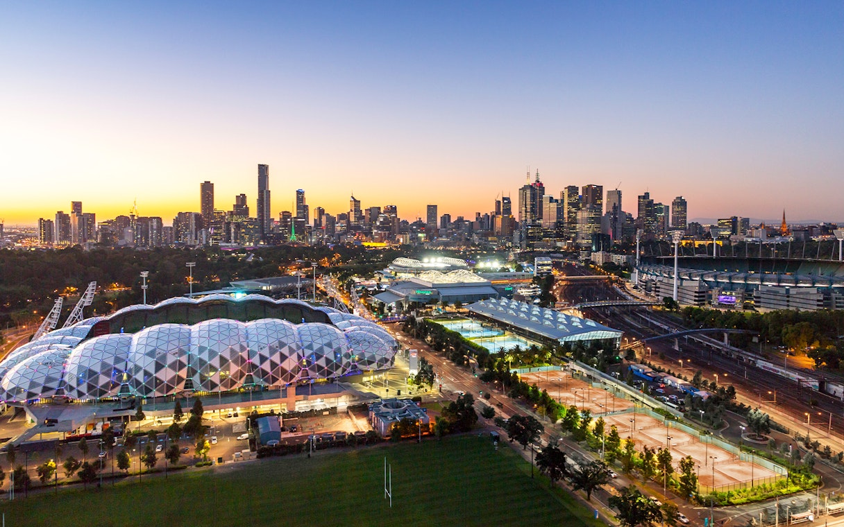 Melbourne skyline with sports venues at sunset, featuring AAMI Park and Melbourne Cricket Ground.