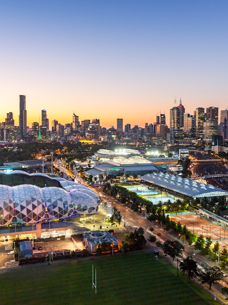 Melbourne skyline with sports venues at sunset, featuring AAMI Park and Melbourne Cricket Ground.