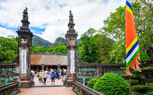 Hoa Lu ancient gate with tourists exploring, surrounded by lush greenery, on the Tam Coc, Hoa Lu & Mua Caves trip.