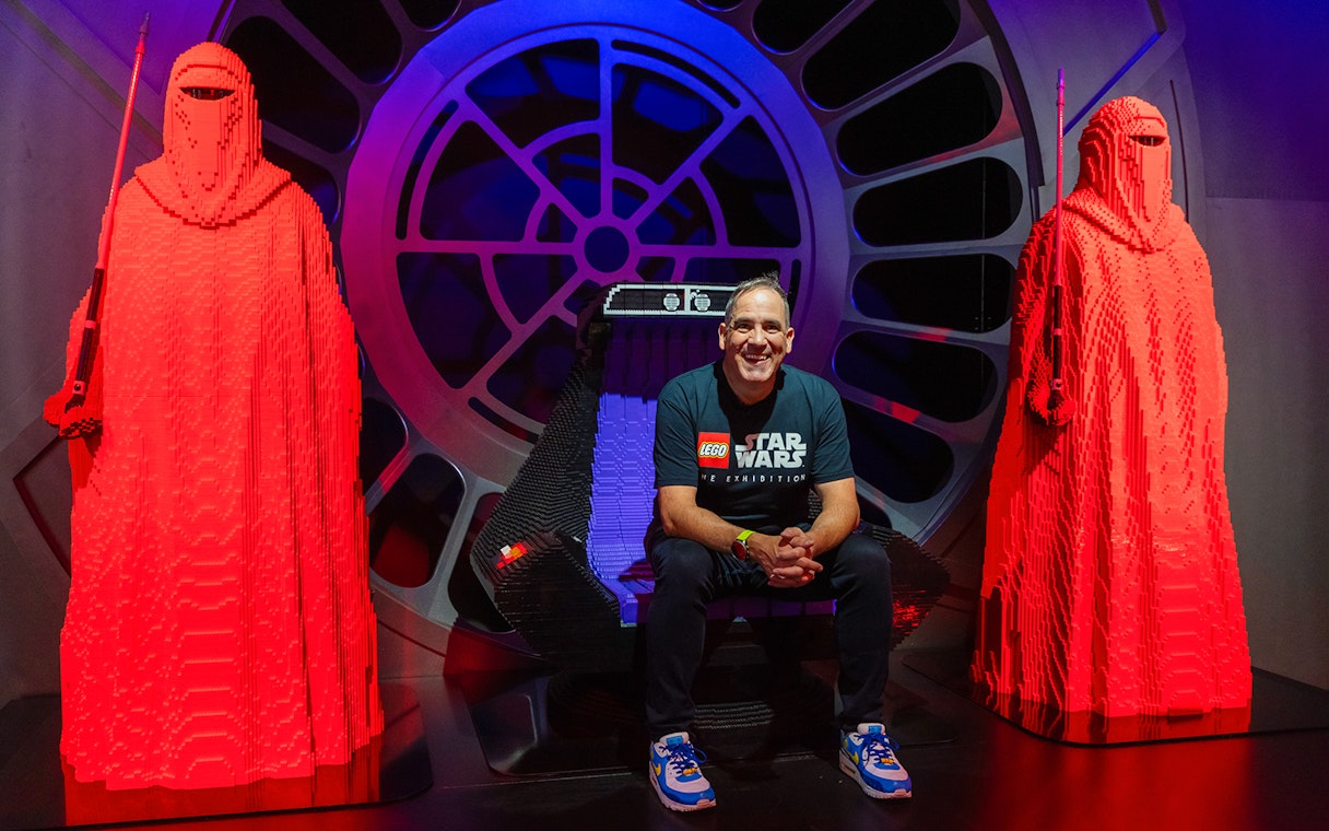 Man sitting on LEGO Emperor's Throne with red LEGO guards, Star Wars exhibition.