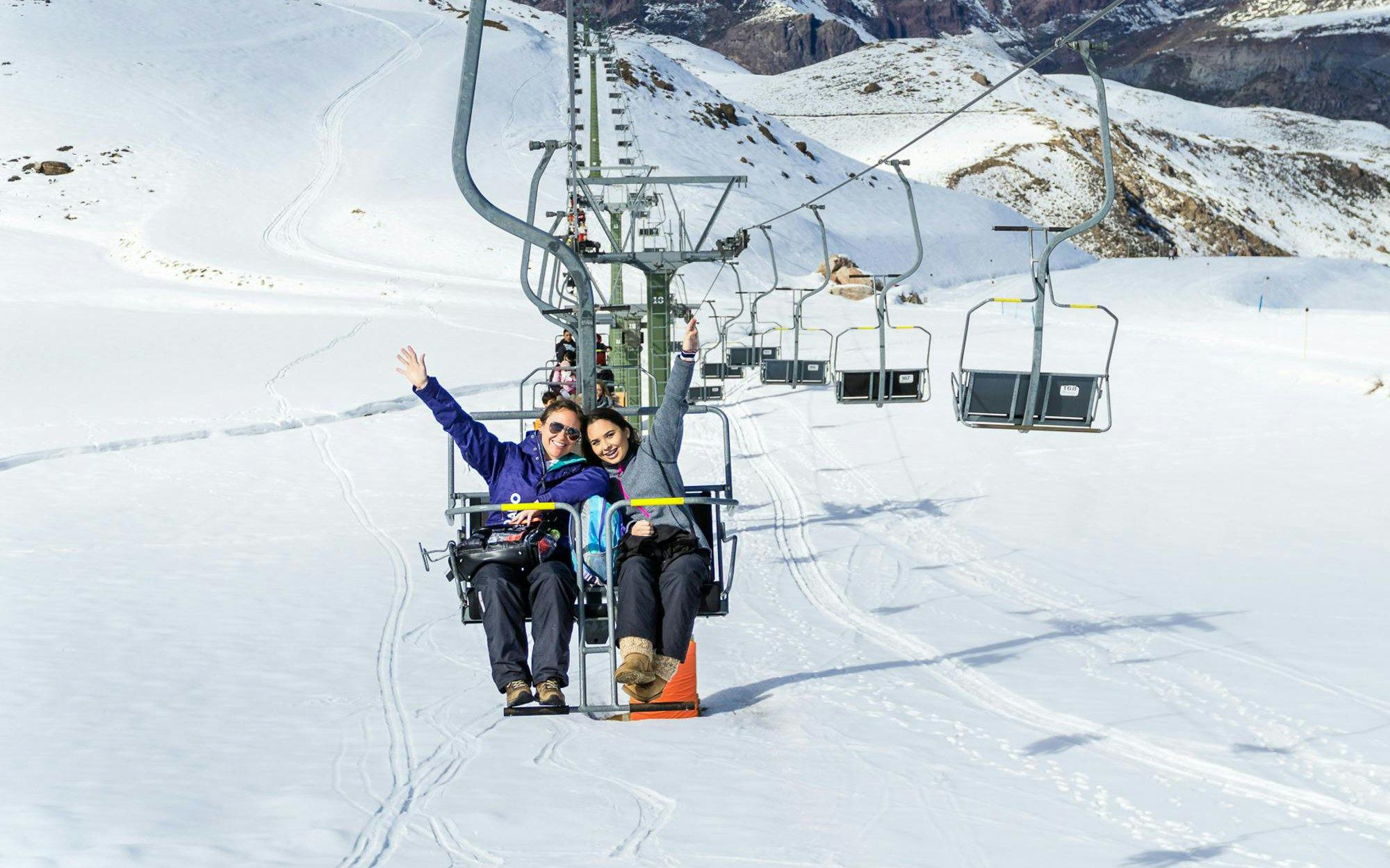 Family on ski lift at Farellones Ski Resort, Chile, with snowy mountains in background.