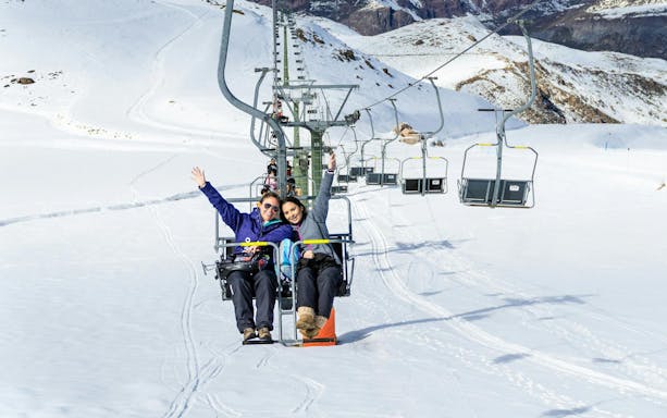 Family on ski lift at Farellones Ski Resort, Chile, with snowy mountains in background.
