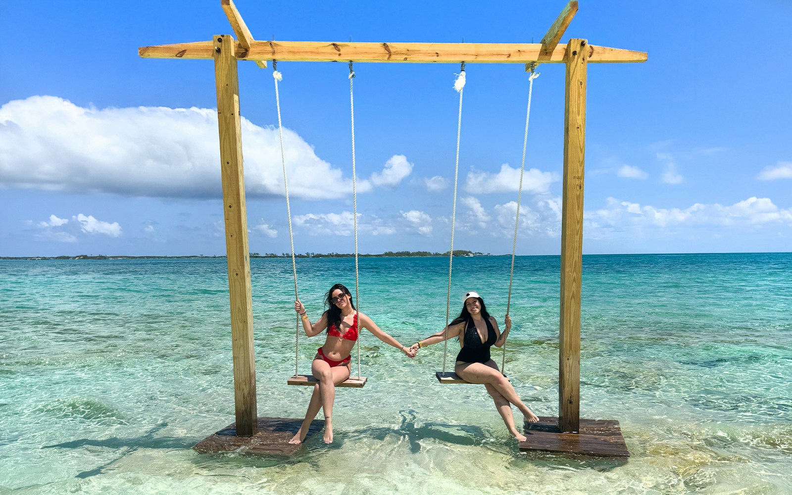 Two people on swings over clear water in Mansa Bay during a private island day trip.