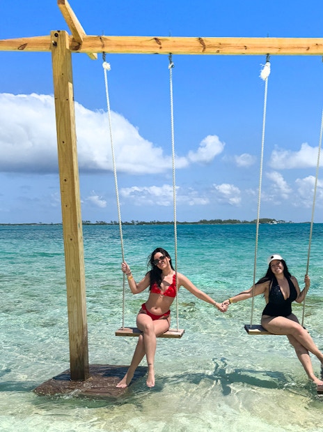 Two people on swings over clear water in Mansa Bay during a private island day trip.