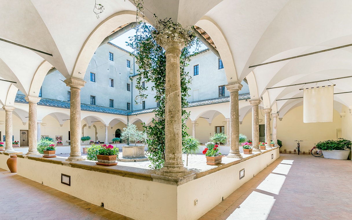 Courtyard of Palazzo Piccolomini with arches and potted plants, part of all-inclusive pass.