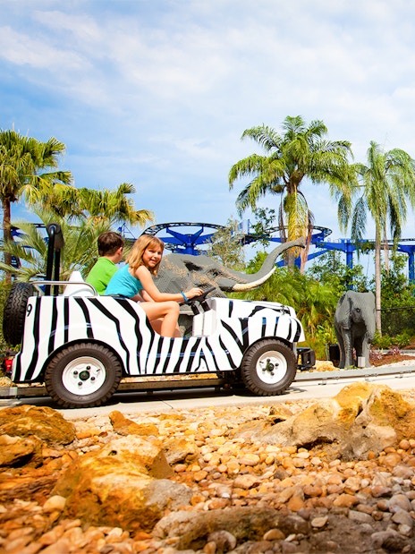 Children riding a zebra-striped vehicle on Safari Trek at LEGOLAND Theme Park, Florida, with LEGO elephants nearby.