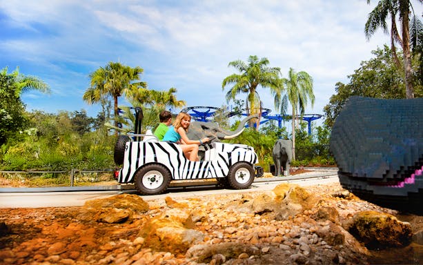 Children riding a zebra-striped vehicle on Safari Trek at LEGOLAND Theme Park, Florida, with LEGO elephants nearby.