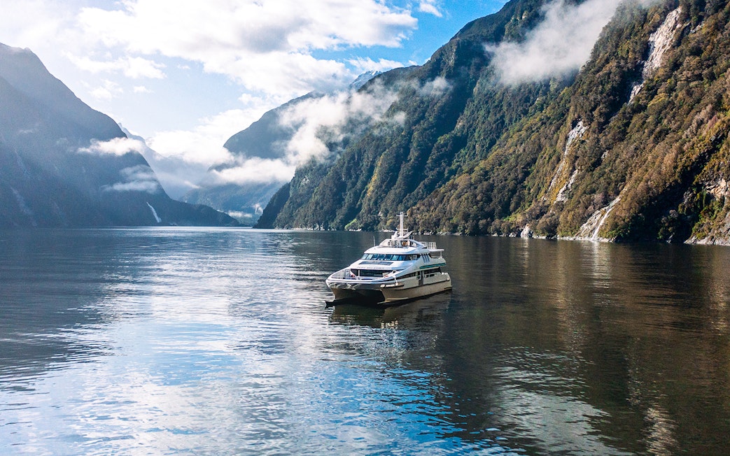 Cruise boat on Milford Sound surrounded by misty mountains and calm waters.
