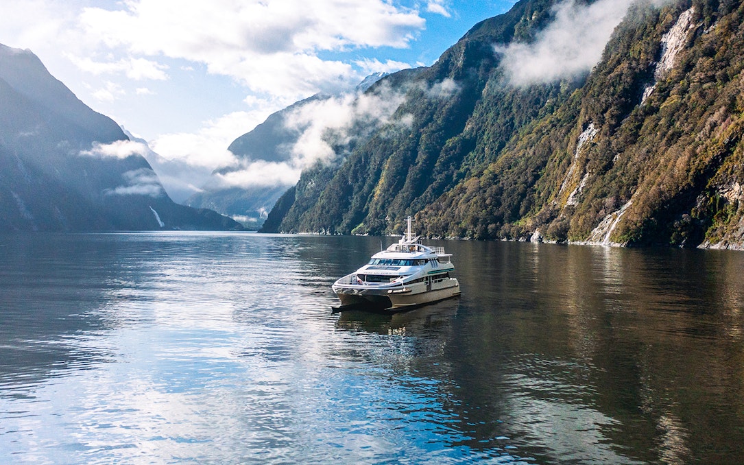 Cruise boat on Milford Sound surrounded by misty mountains and calm waters.