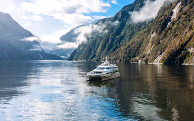 Cruise boat on Milford Sound surrounded by misty mountains and calm waters.