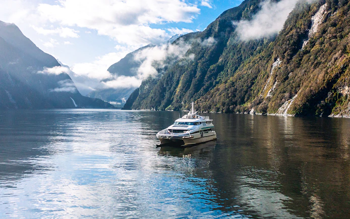 Cruise boat on Milford Sound surrounded by misty mountains and calm waters.