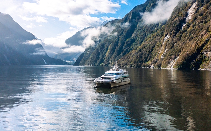 Cruise boat on Milford Sound surrounded by misty mountains and calm waters.