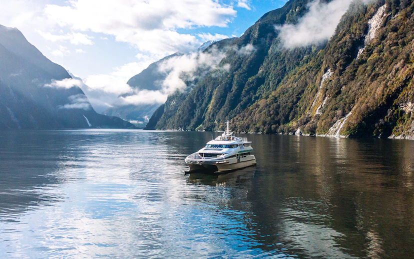 Cruise boat on Milford Sound surrounded by misty mountains and calm waters.