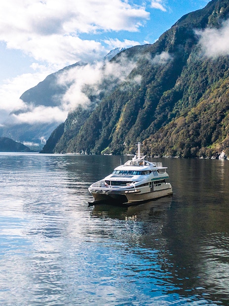 Cruise boat on Milford Sound surrounded by misty mountains and calm waters.