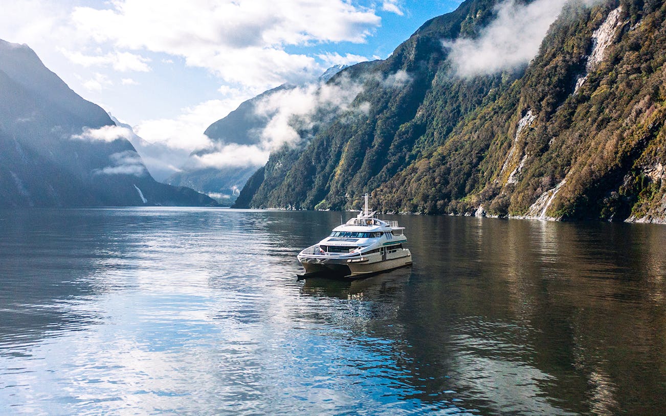 Cruise boat on Milford Sound surrounded by misty mountains and calm waters.