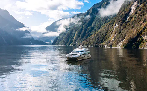 Cruise boat on Milford Sound surrounded by misty mountains and calm waters.