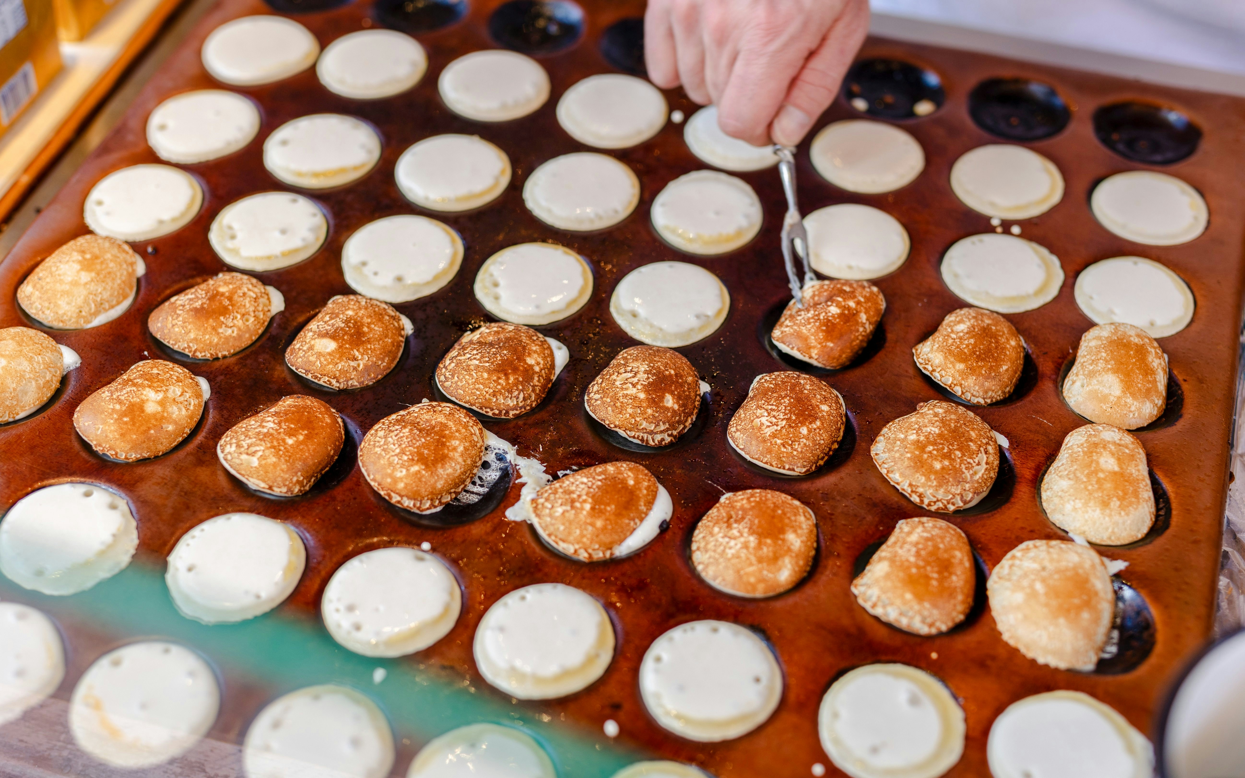 Cooking poffertjes, traditional Dutch mini pancakes, on a hot griddle.