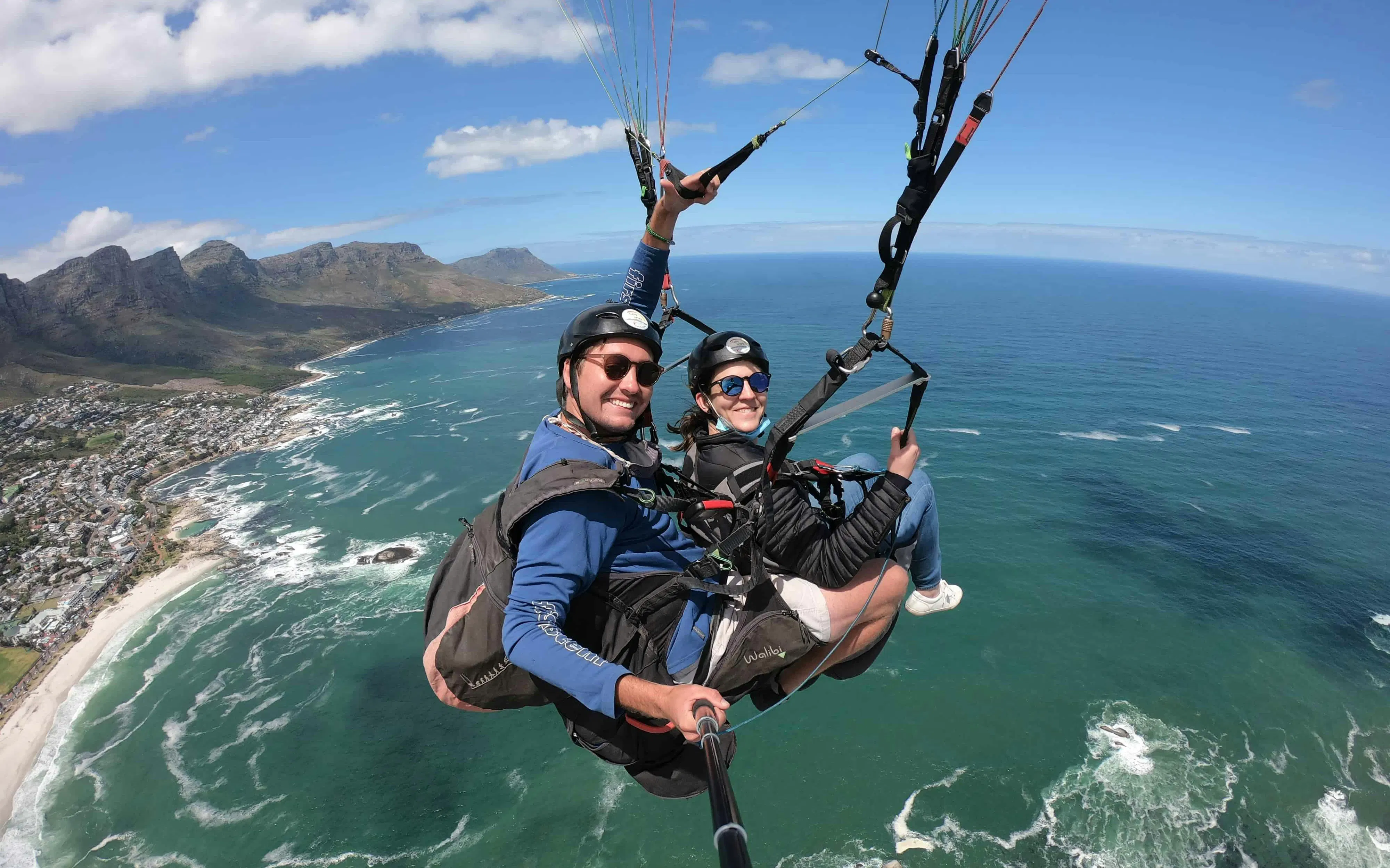 Tandem paragliding over Cape Town coastline with ocean and mountains in view.