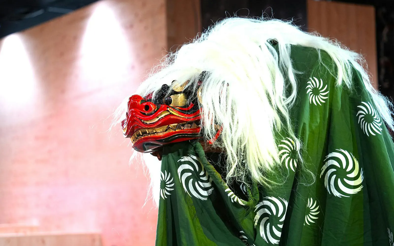 Shishimai lion dance costume with red mask and green cloak at sumo event in Japan.