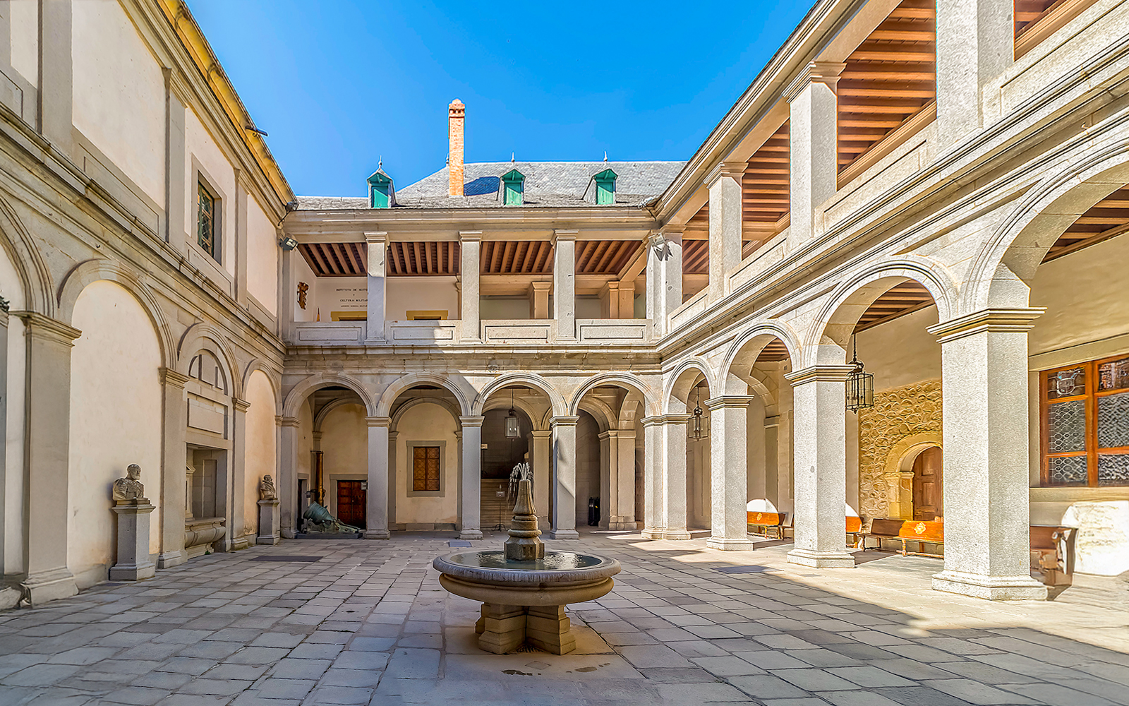 Central courtyard of the Alcázar of Segovia with stone arches and a central fountain.