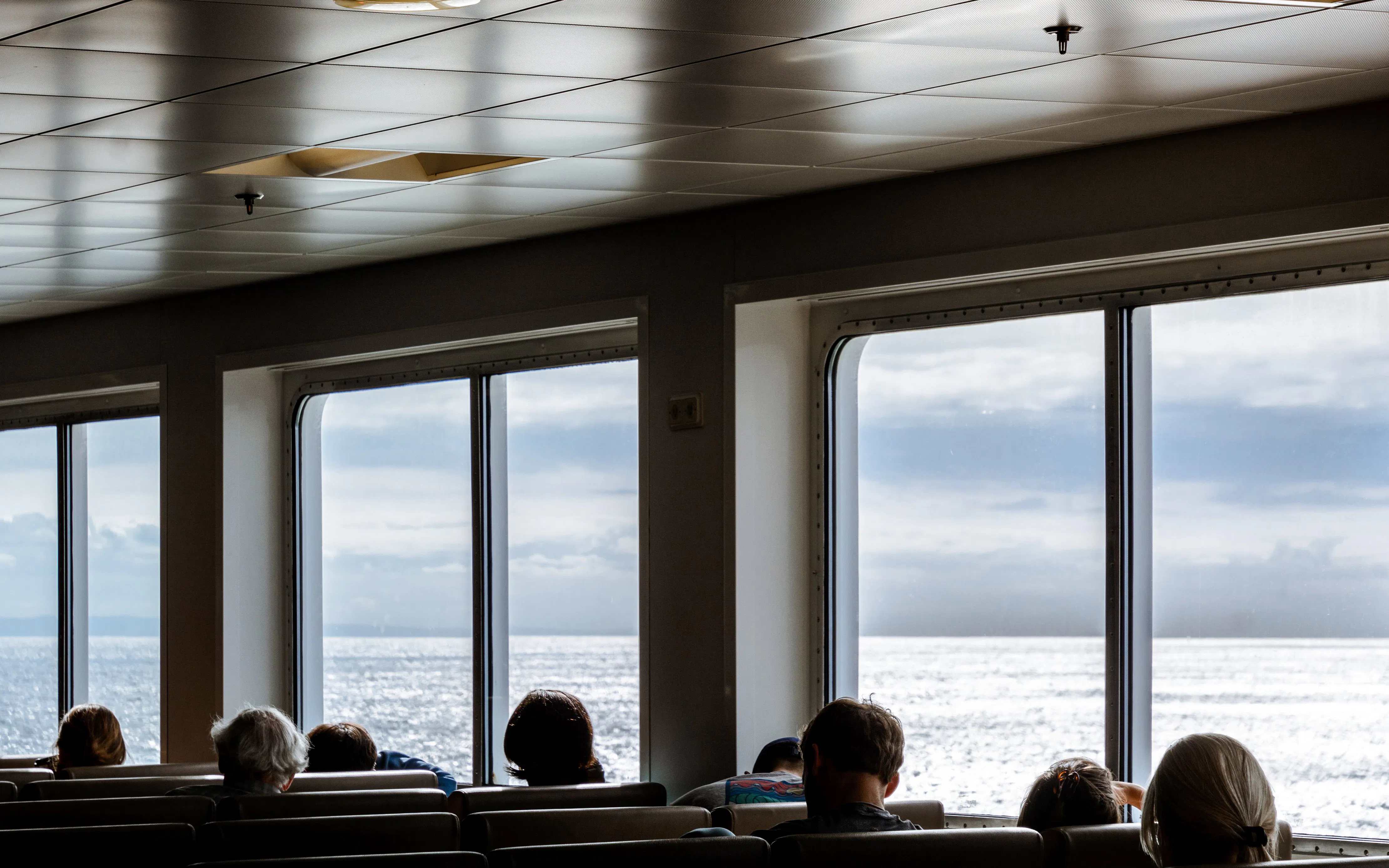 Indoor boat passengers seated by large windows with ocean view.