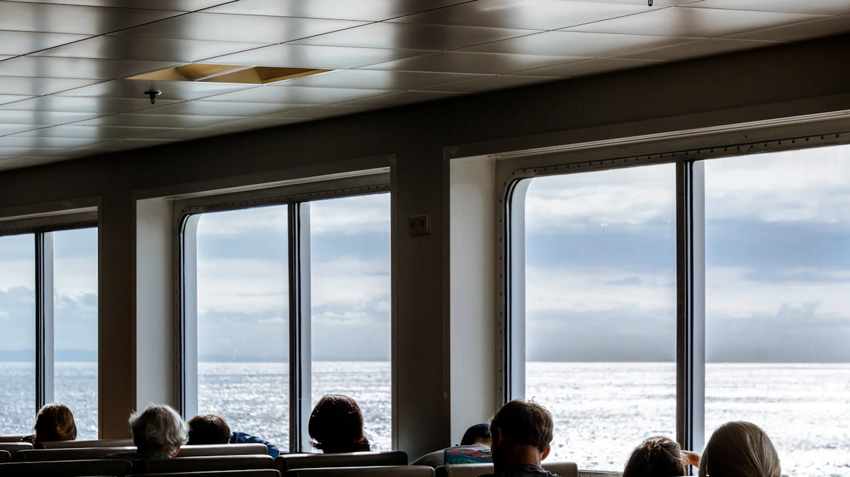 Indoor boat passengers seated by large windows with ocean view.