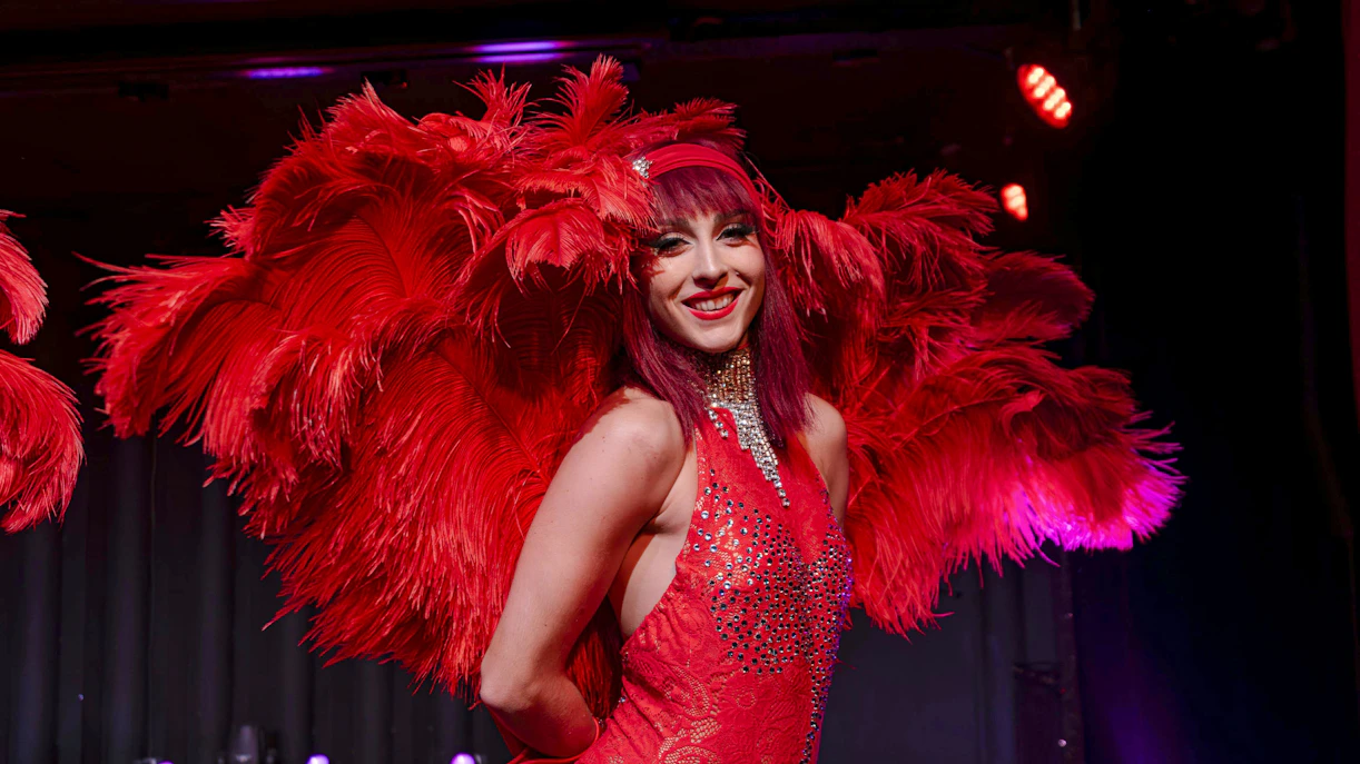 Performer in red feather costume at Les Nuits de Lola Oh Cesar show, France.