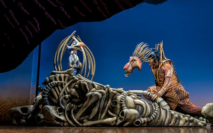 Stage performance of The Lion King with actors in elaborate costumes.