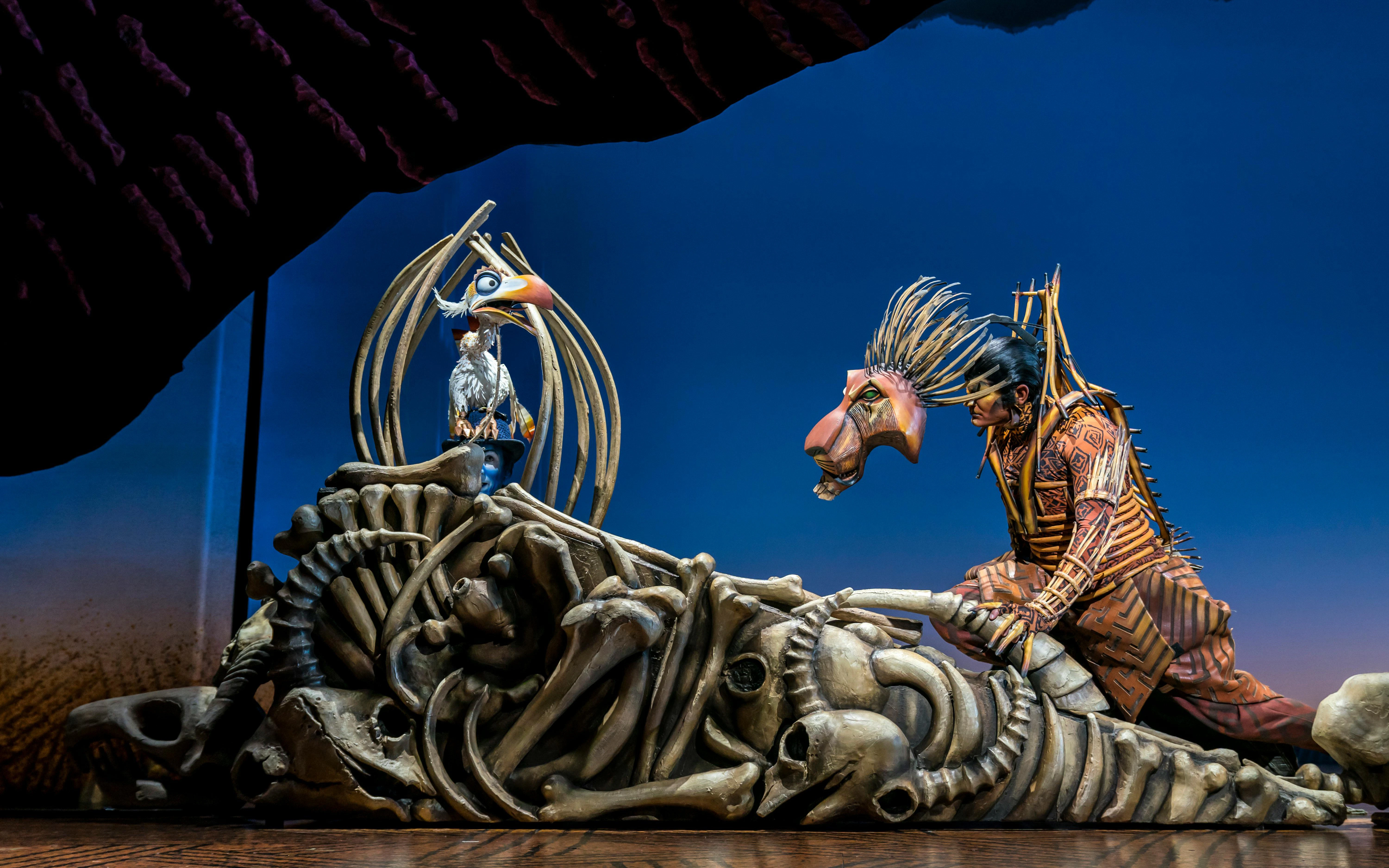 Stage performance of The Lion King with actors in elaborate costumes.