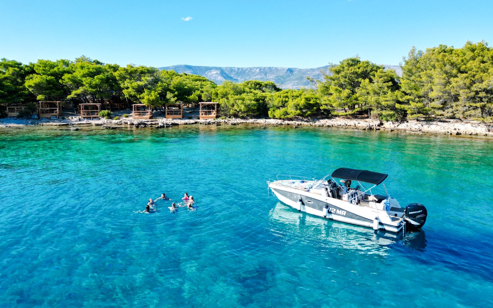 Guests swimming near speedboat in Blue Lagoon, Hvar, surrounded by lush greenery.