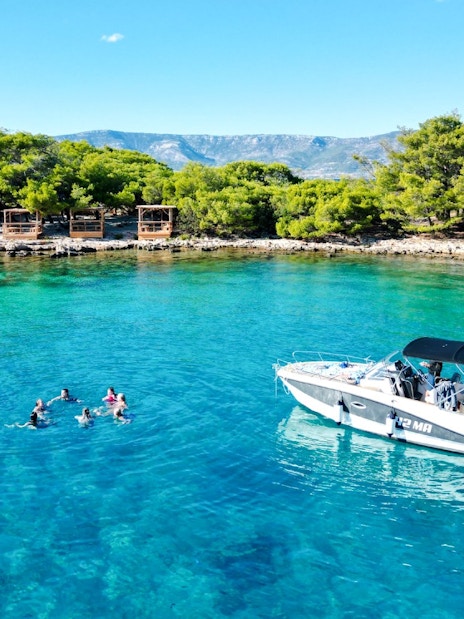 Guests swimming near speedboat in Blue Lagoon, Hvar, surrounded by lush greenery.