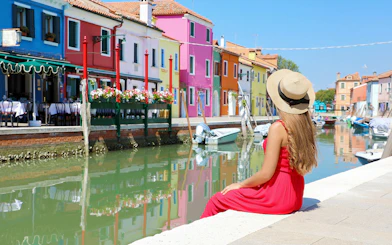 Girl admiring colorful buildings along a canal in Murano, Italy.