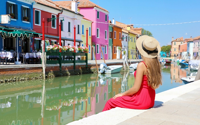 Girl admiring colorful buildings along a canal in Murano, Italy.