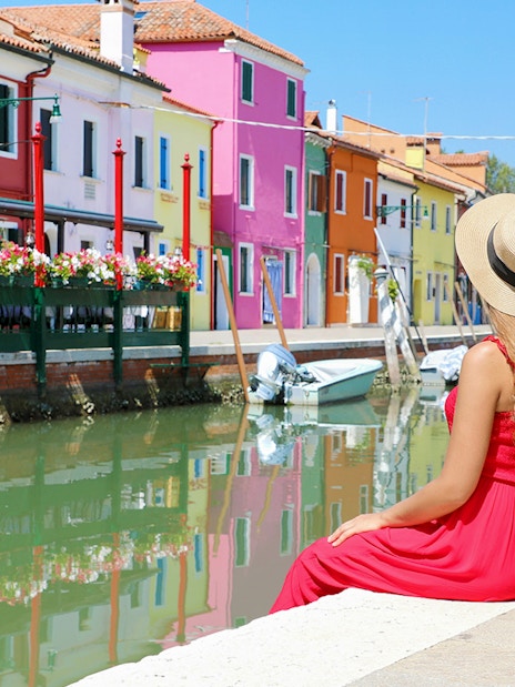 Girl admiring colorful buildings along a canal in Murano, Italy.